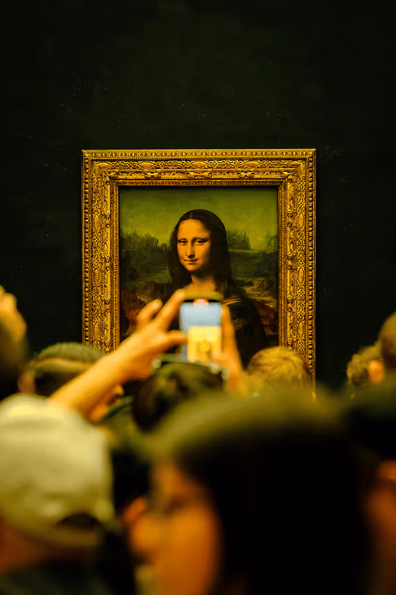 People taking photos with phones of the Mona Lisa painting in a museum, with hands holding devices visible in foreground and the famous artwork in ornate gold frame in background.