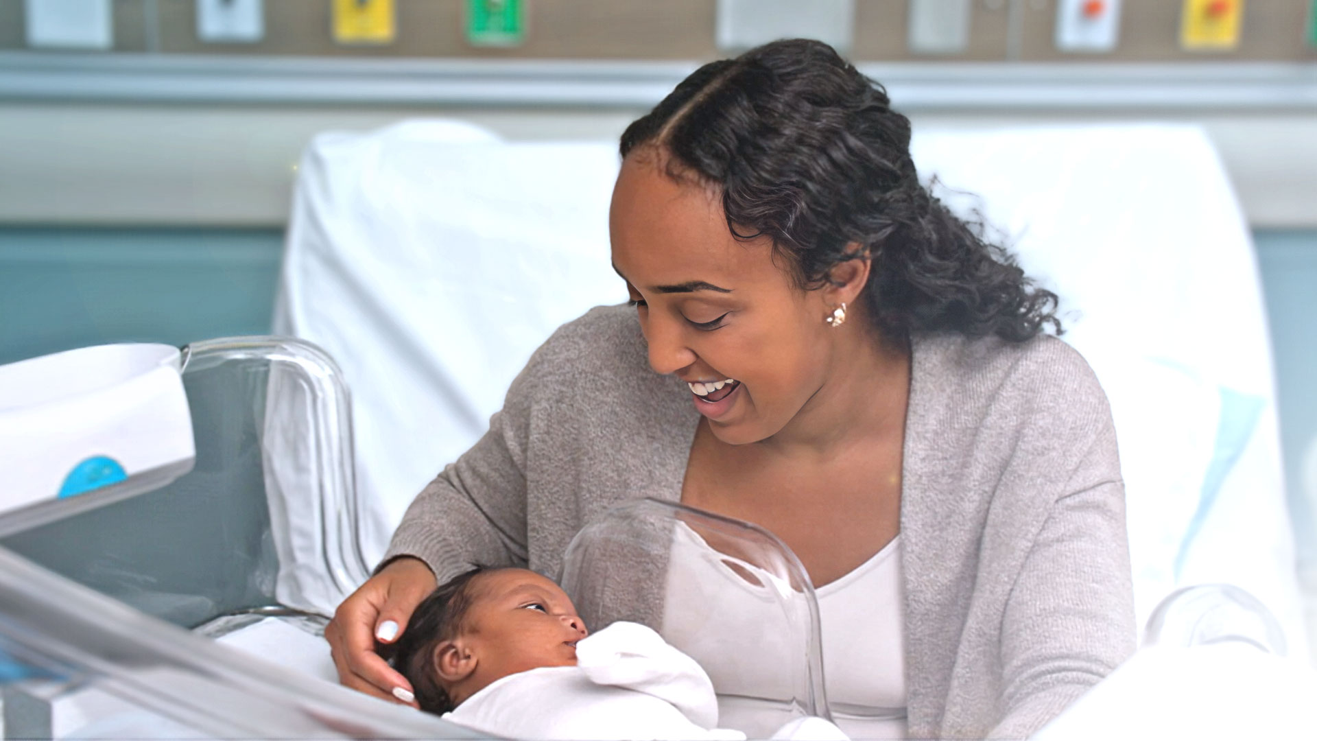 A smiling mother reaching into the Couplet Care Bassinet to comfort infant 