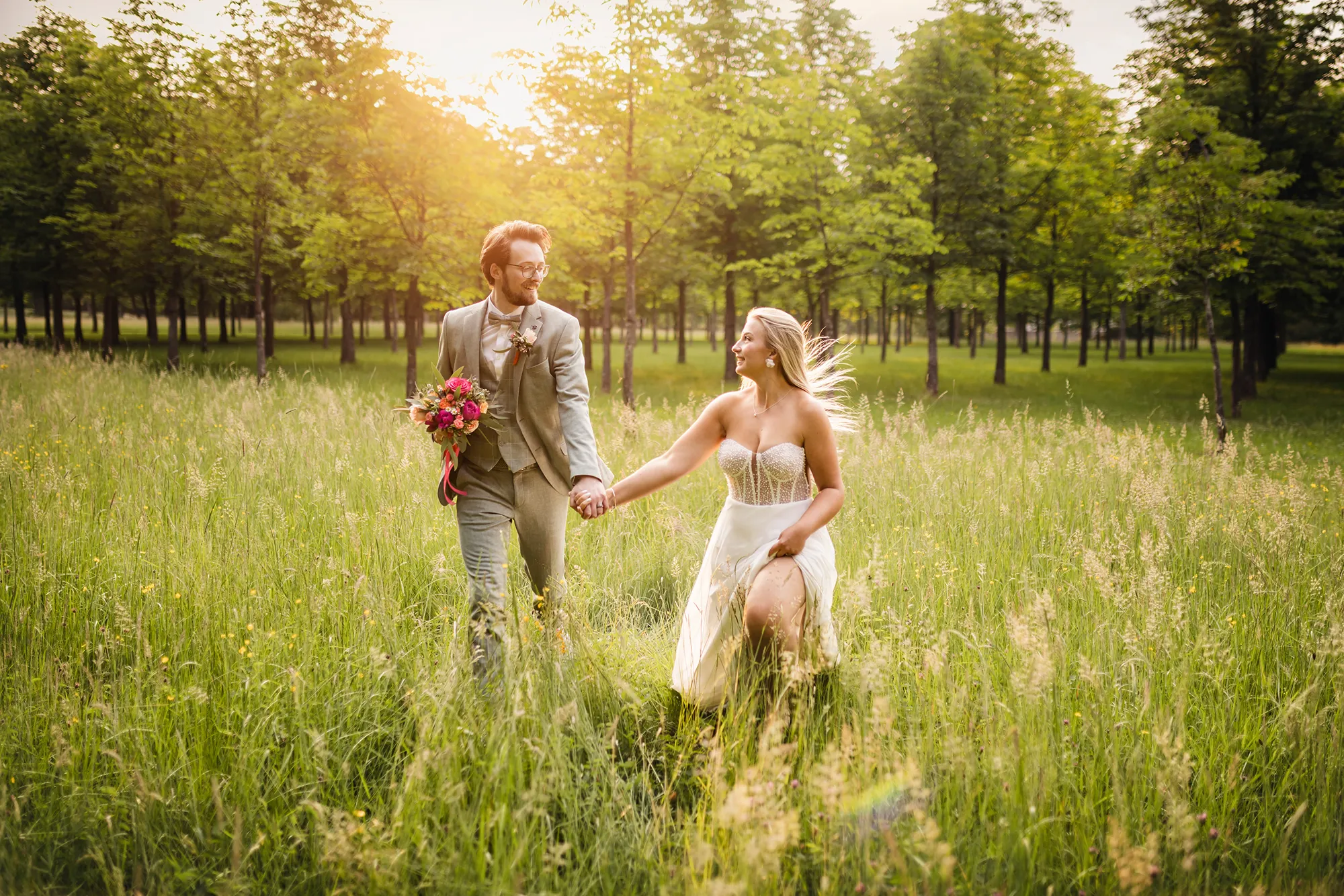 Hochzeitspaar, das Hand in Hand über eine Wiese läuft.