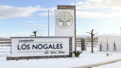 Un lindo letrero que dice "Campestre Los Nogales de San Jose." Tiene el logotipo de un arbol abstracto. Tiene acabados de piedra. A los lados se encuentran dos arboles sin hojas y se puede ver nieve todo alrededor.