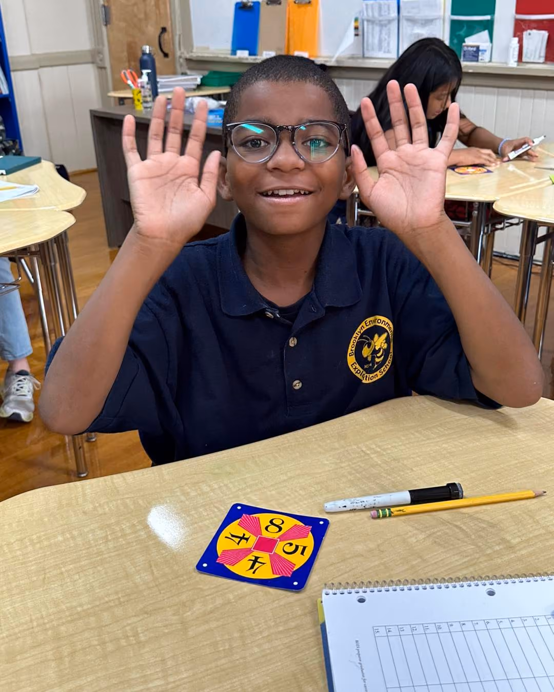 Student in uniform raises both hands smiling during math class