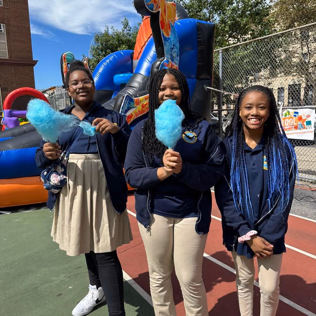 Three students in school uniforms holding blue cotton candy at outdoor fair