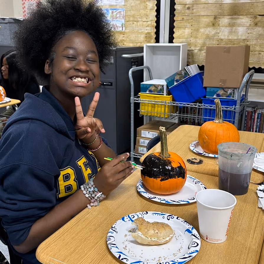 Student smiling and painting a pumpkin during classroom fall activity