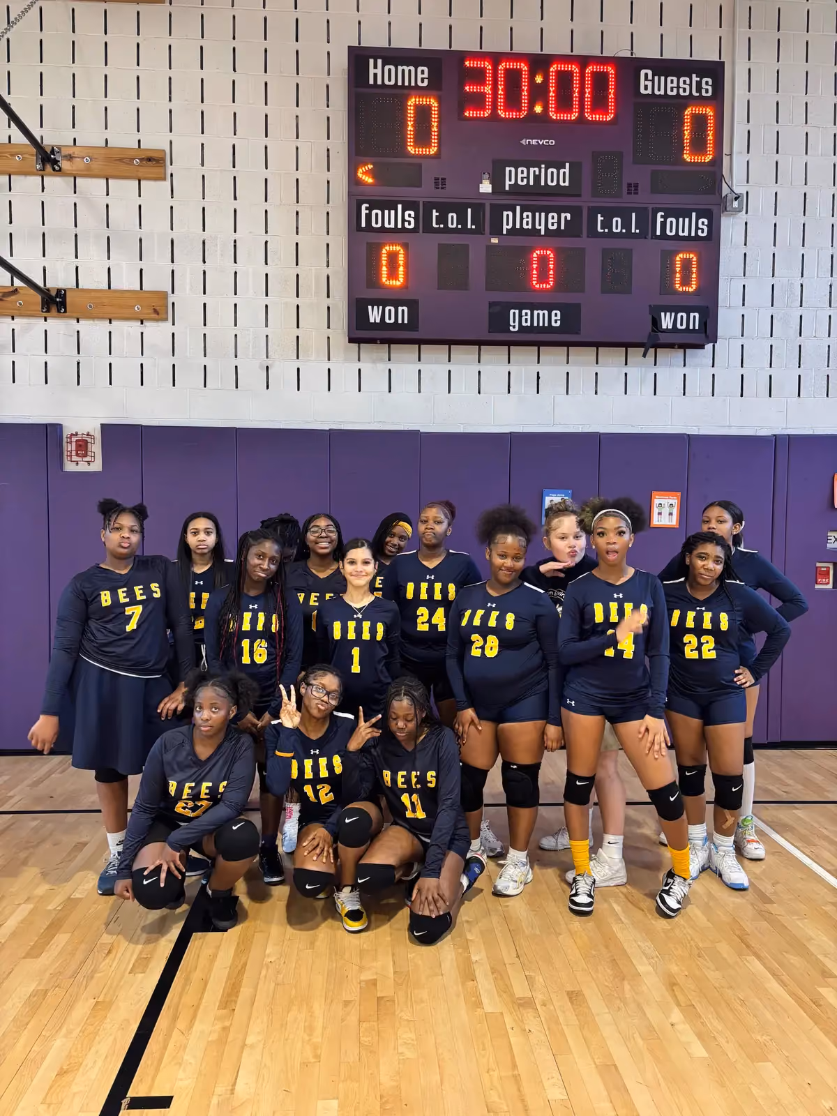 Bees girls volleyball team posing together in school gymnasium