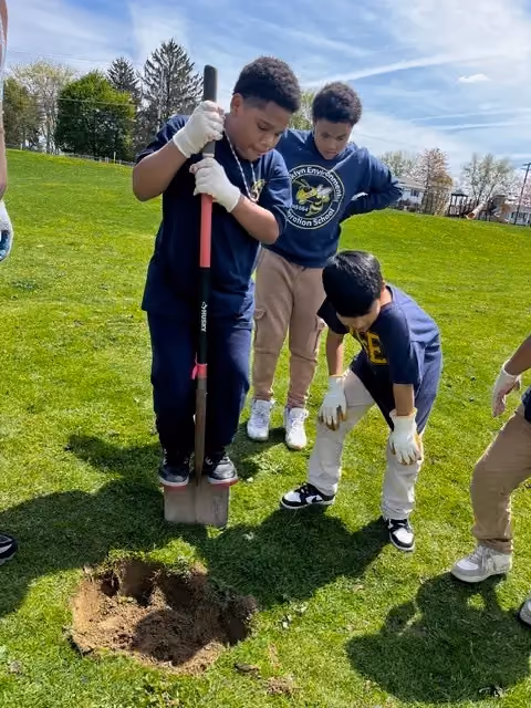 Students digging a hole in a school field wearing gloves