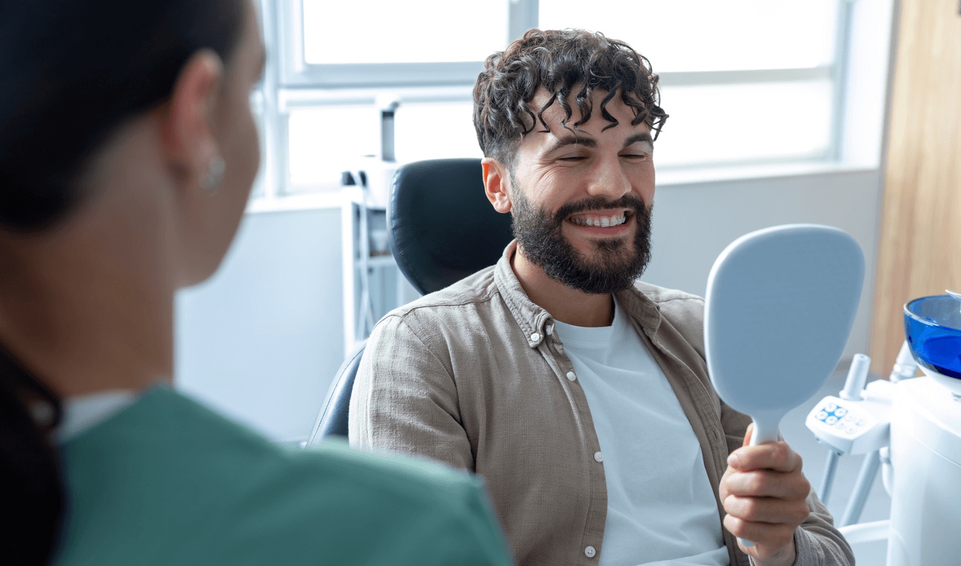 A young adult wearing clear braces looks in the mirror at the best orthodontist in Redwood City