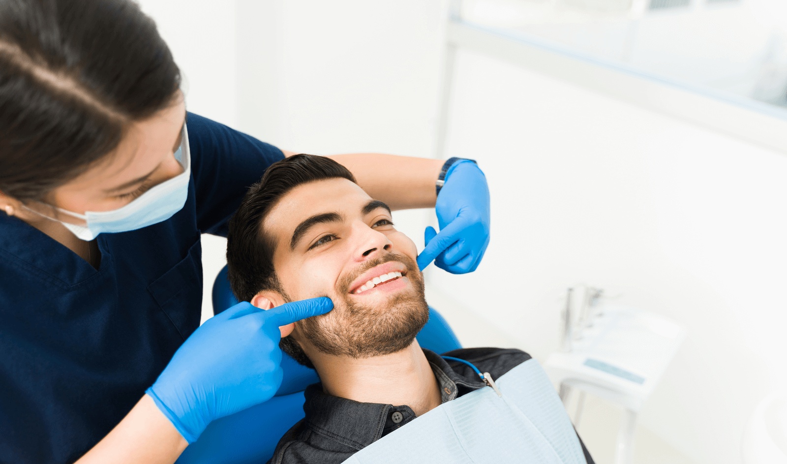 The best dentist in Redwood City, CA, is examining a smiling patient in the dental chair during a cosmetic dentistry evaluation.