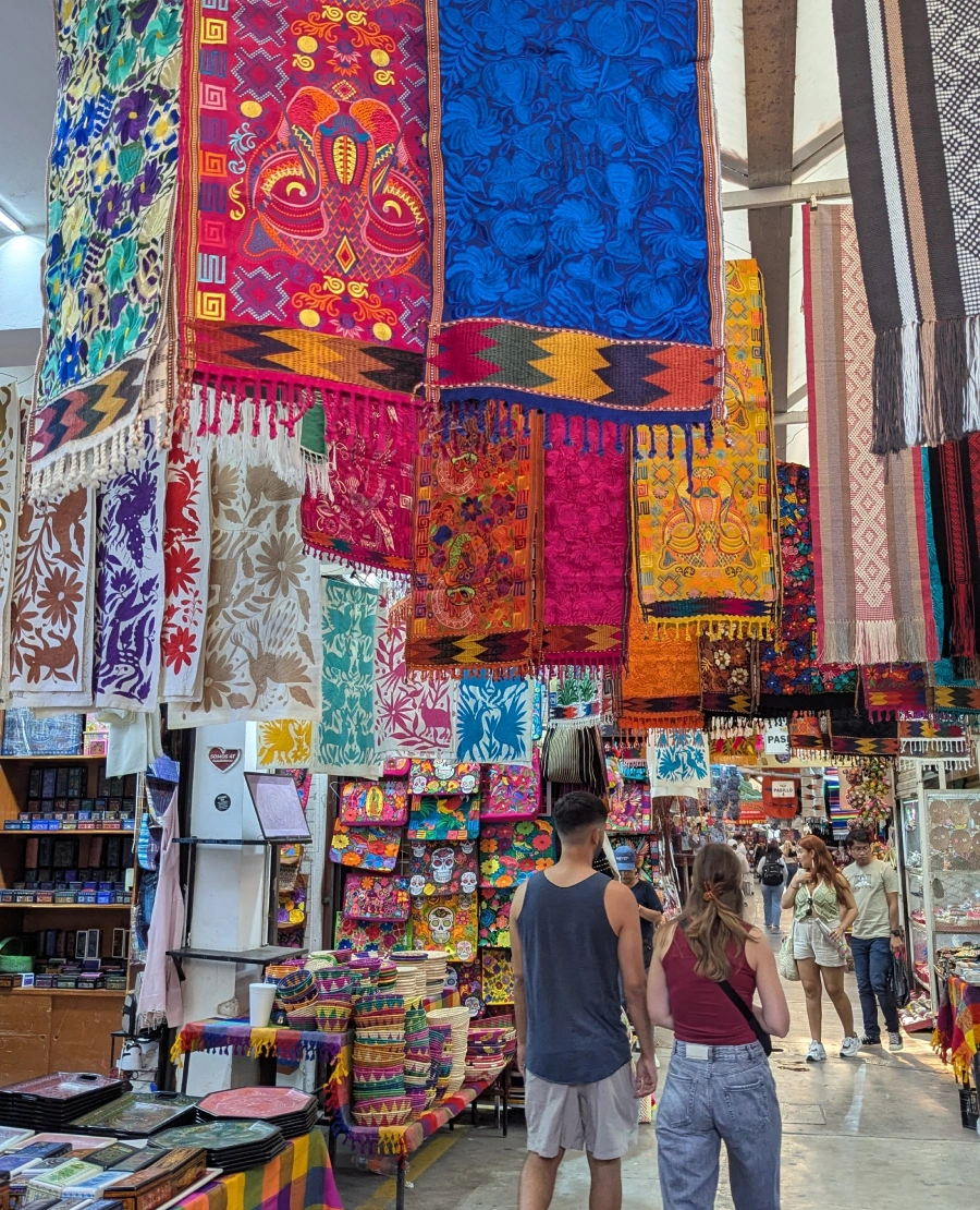 Colorful fabrics hang from the ceiling at a Mexican market