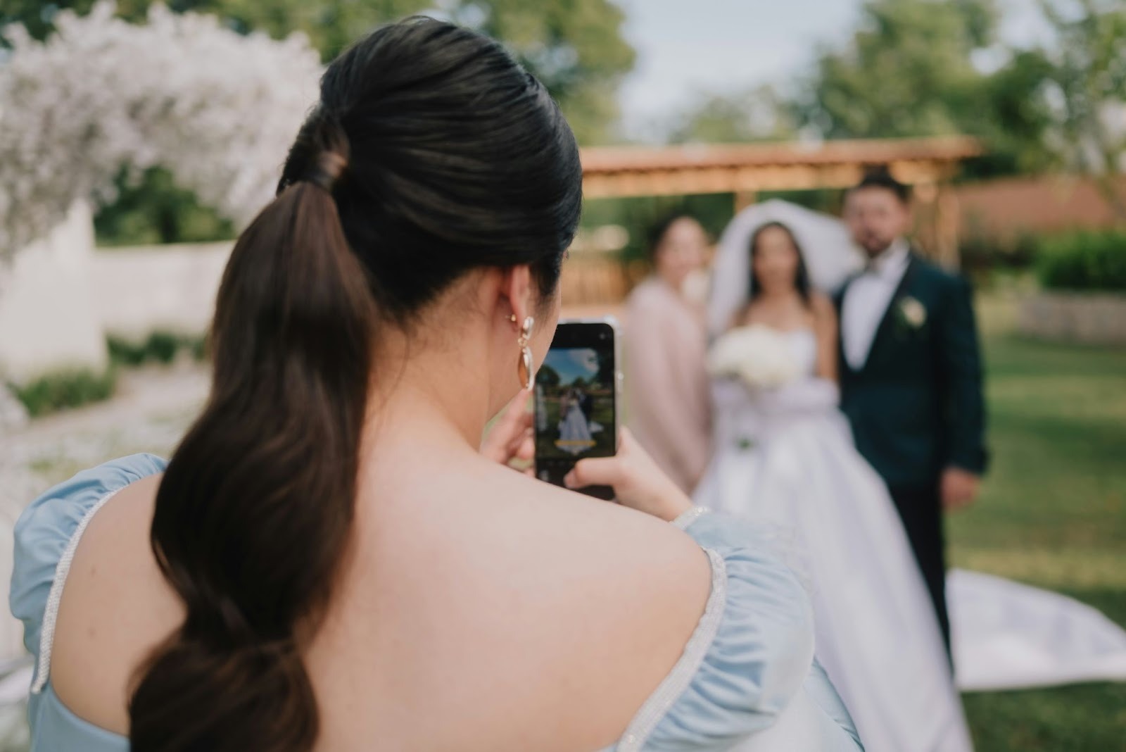 A woman taking a photo of a bride and groom rom her mobile phone