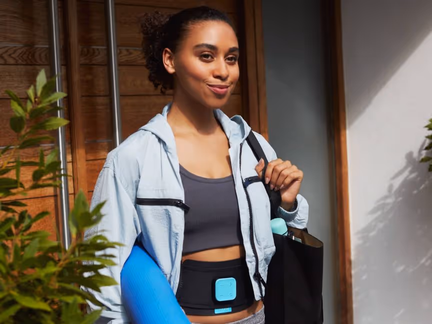 women wearing a slendertone device and carrying a light blue yoga mat 