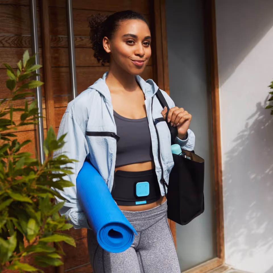 women wearing a slendertone device and carrying a light blue yoga mat 