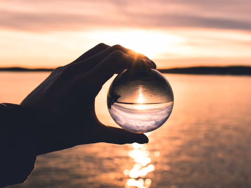 Hand holding glass globe showing the reflection of the sea landscape.