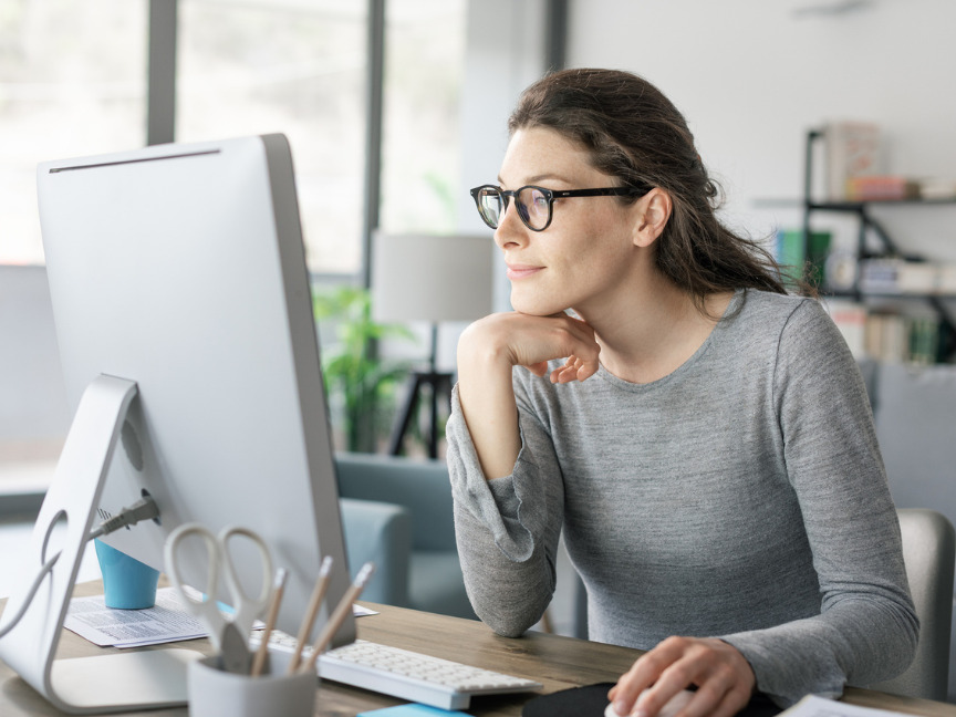 A woman seated at her desk, focused on her computer while working from home.