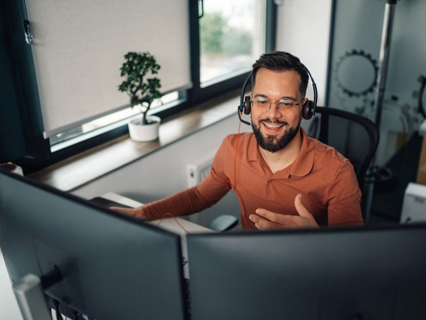 Man working from home wearing headset in front of two screens