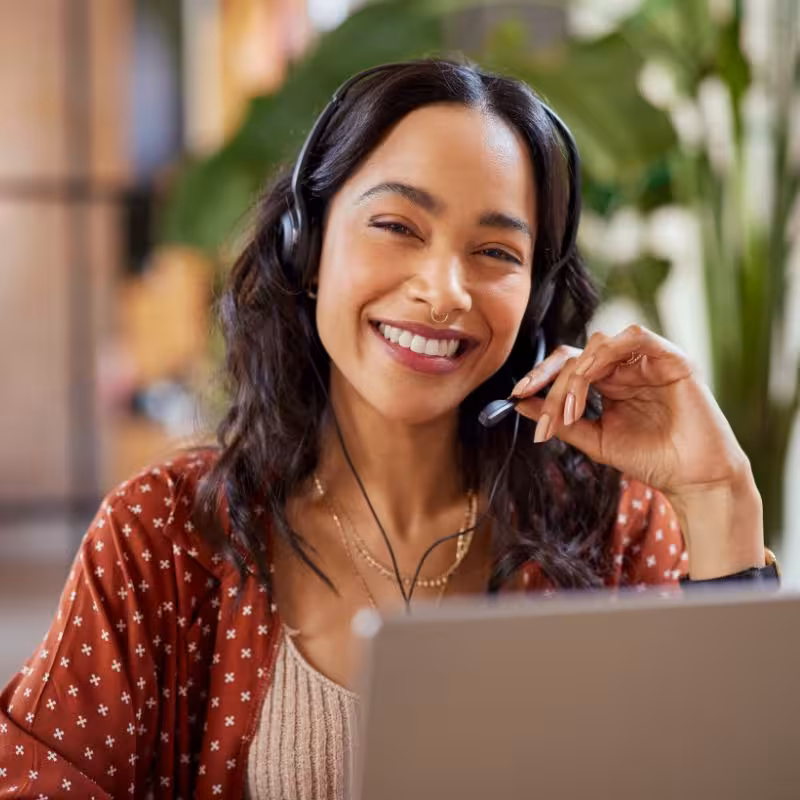 BPO customer experience agent looking at the camera smiling while using headset to take call from client.