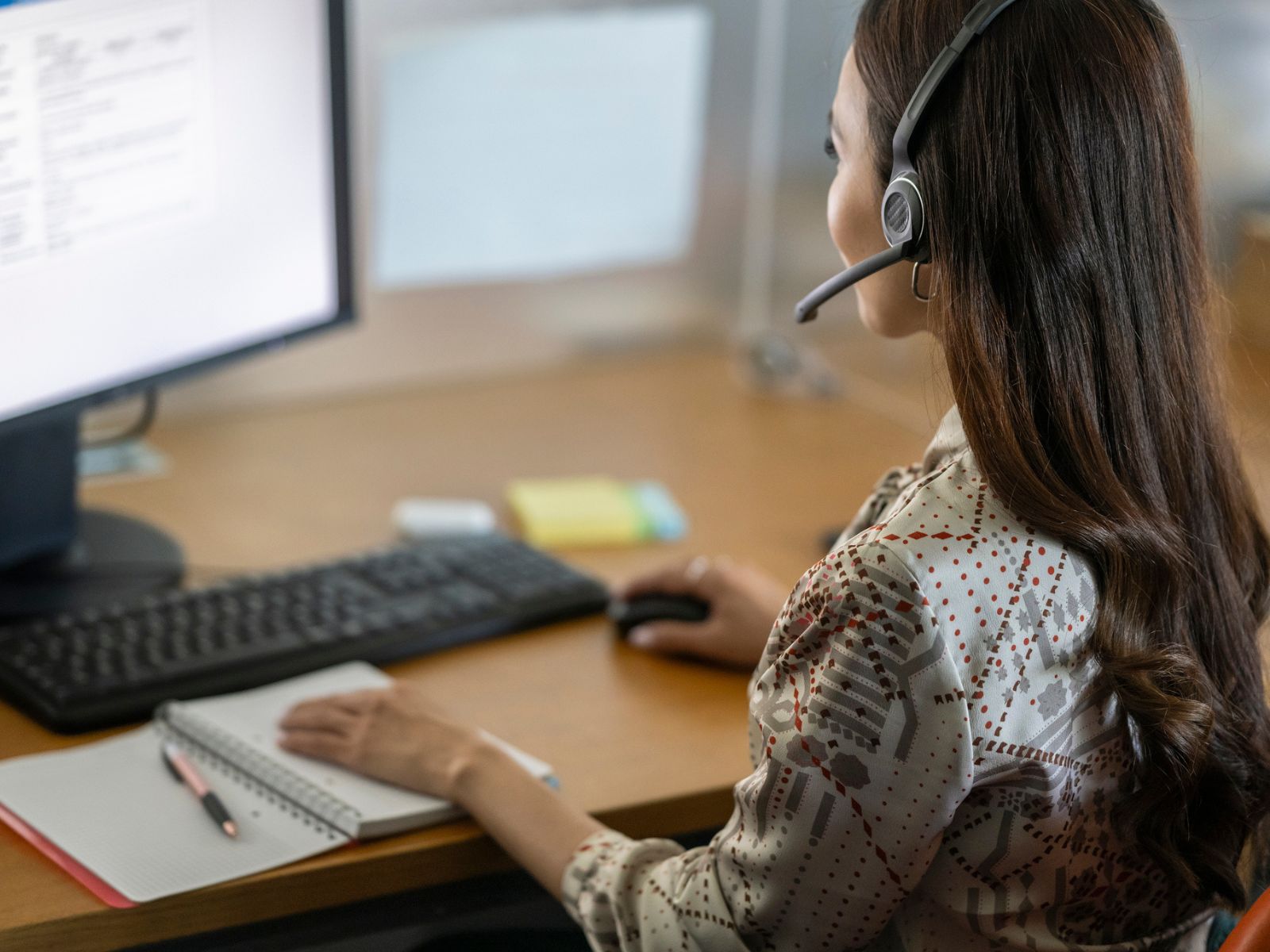Woman seated at her desk wearing headphones in front of her computer