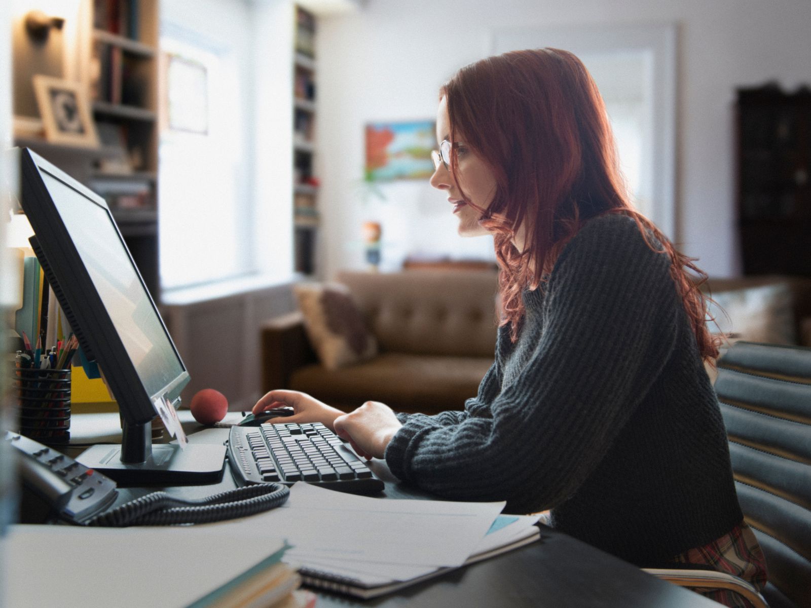women working in her home office, sitting at her desk, profile side view.