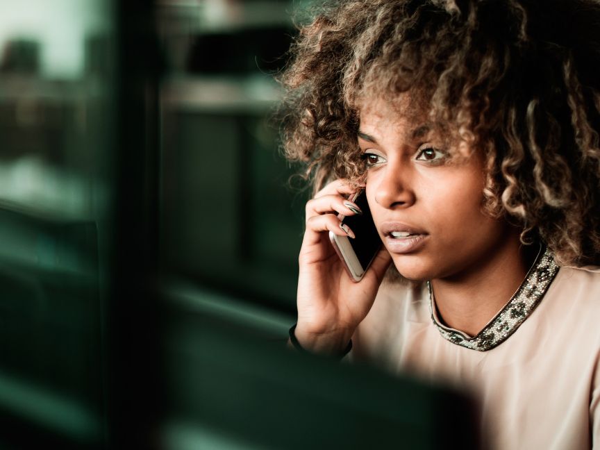 Young women at work, talking on the phone while sitting at desk.