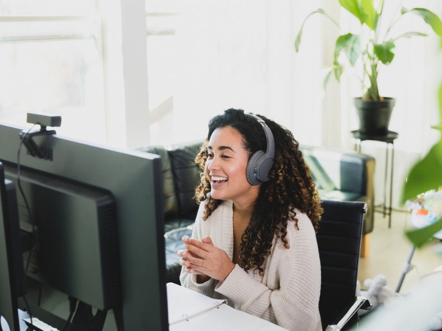 Woman sitting at her home office desk looking at computer with headphones on