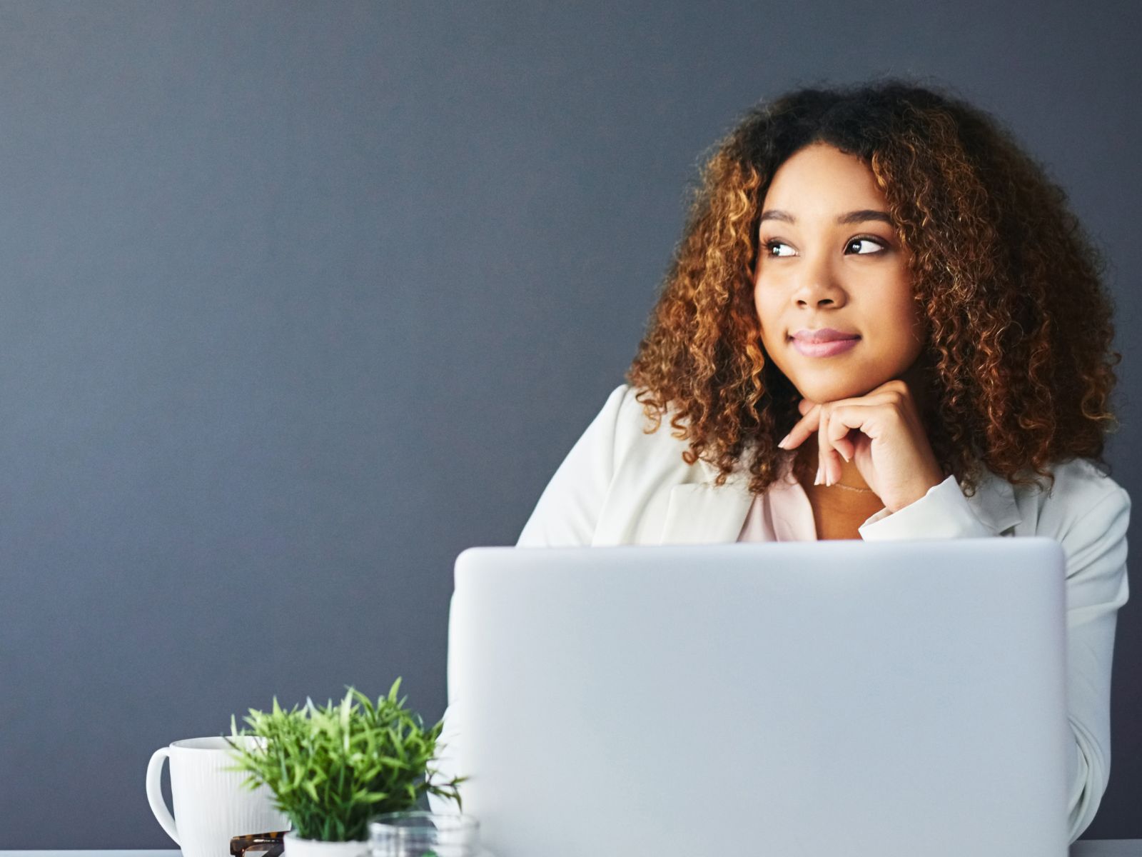 Woman sitting at desk with computer open looking to the left on dark background