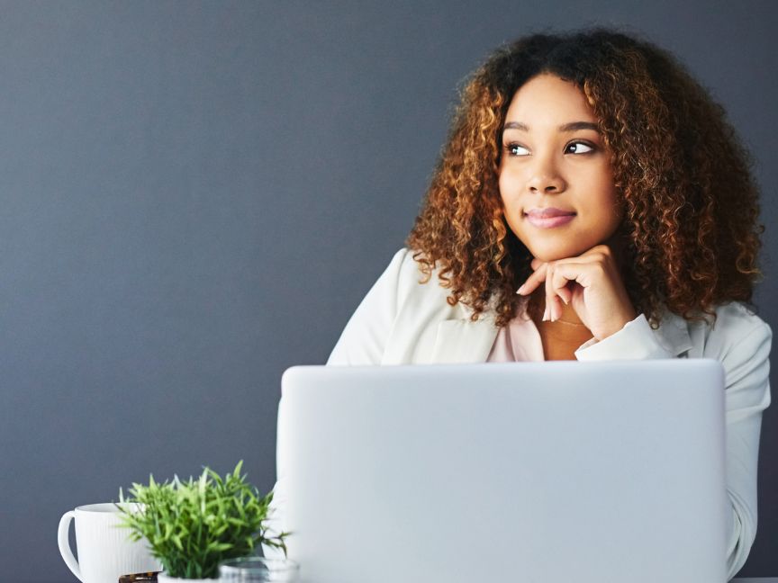 Woman sitting at desk with computer open looking to the left on dark background