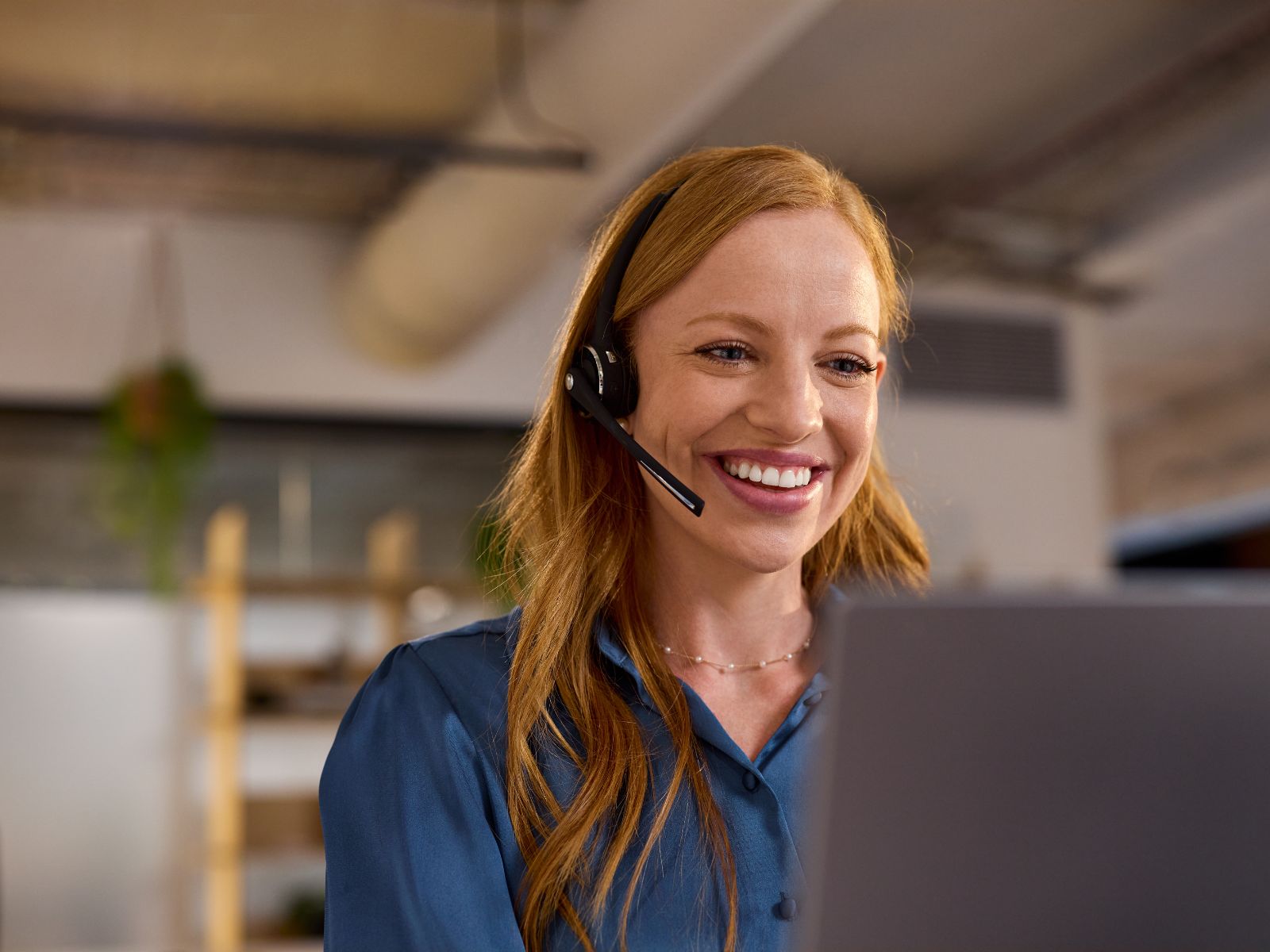 Woman at desk wearing headphones in front of computer, smiling, facing camera