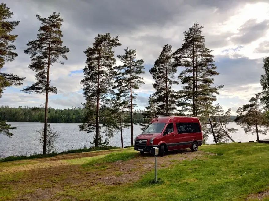 Der rote Camping-App-Van steht am See in Schweden