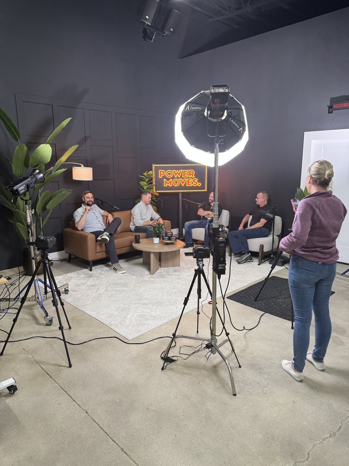 Four people recording a panel discussion in the Noir Lounge under a large softbox while a camera operator films