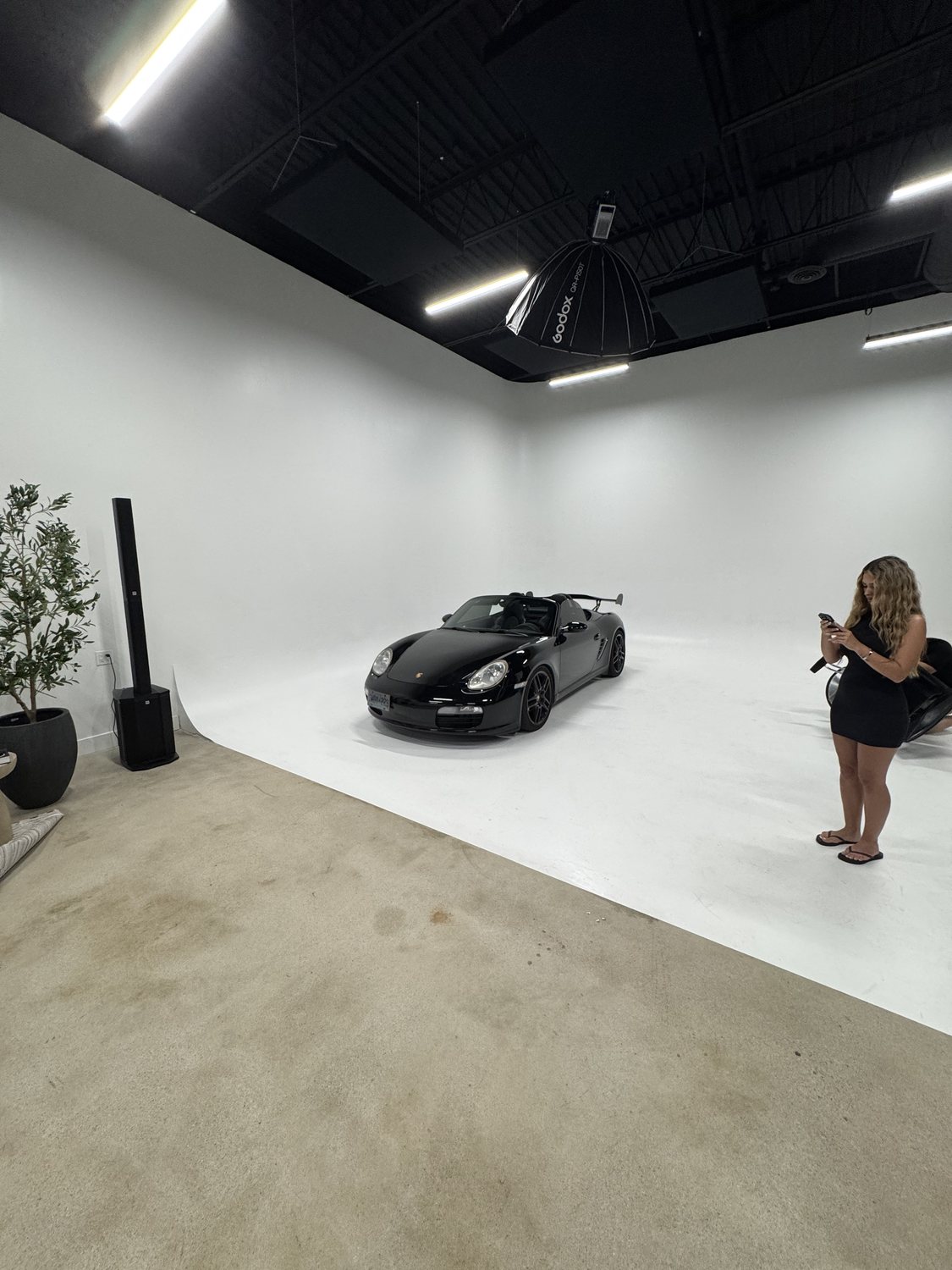 A black sports car parked on the white cyclorama wall while a photographer shoots it under a softbox