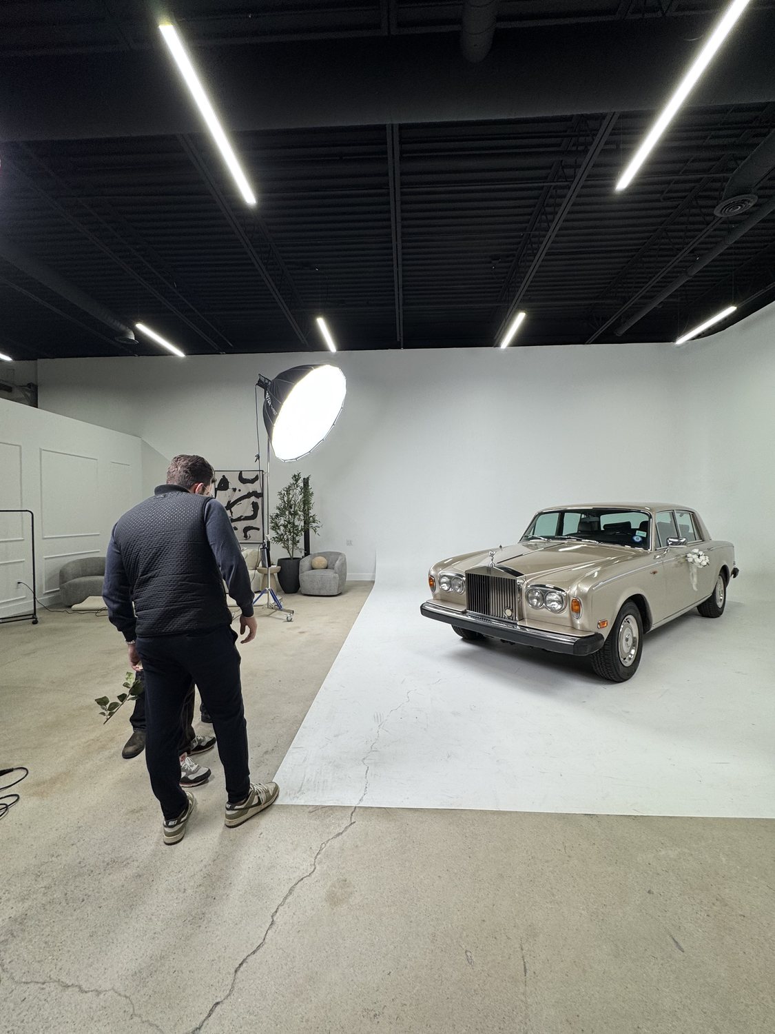 A classic car parked on the white cyclorama wall with a beauty dish light and crew standing by