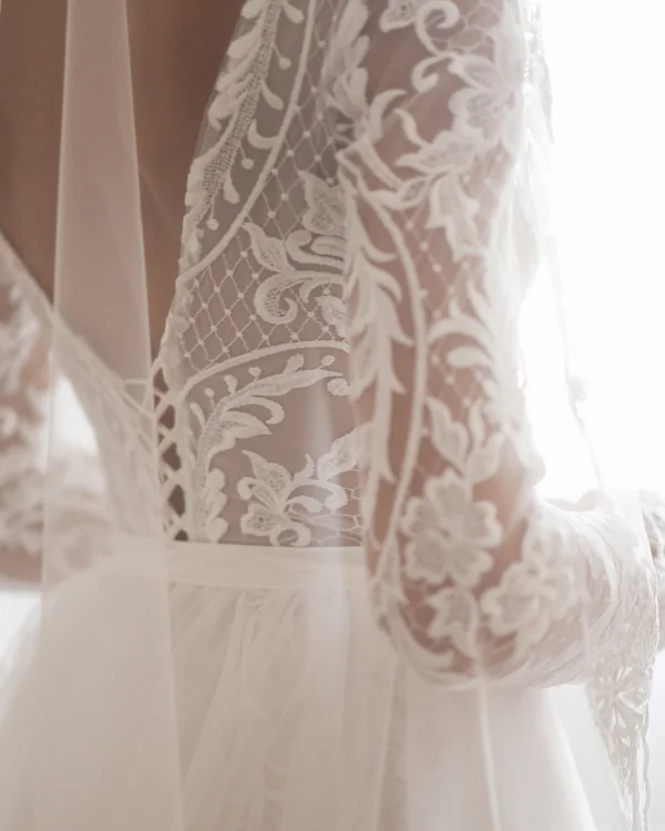 Close-up of a white lace wedding dress with intricate floral and leaf patterns on sheer fabric.