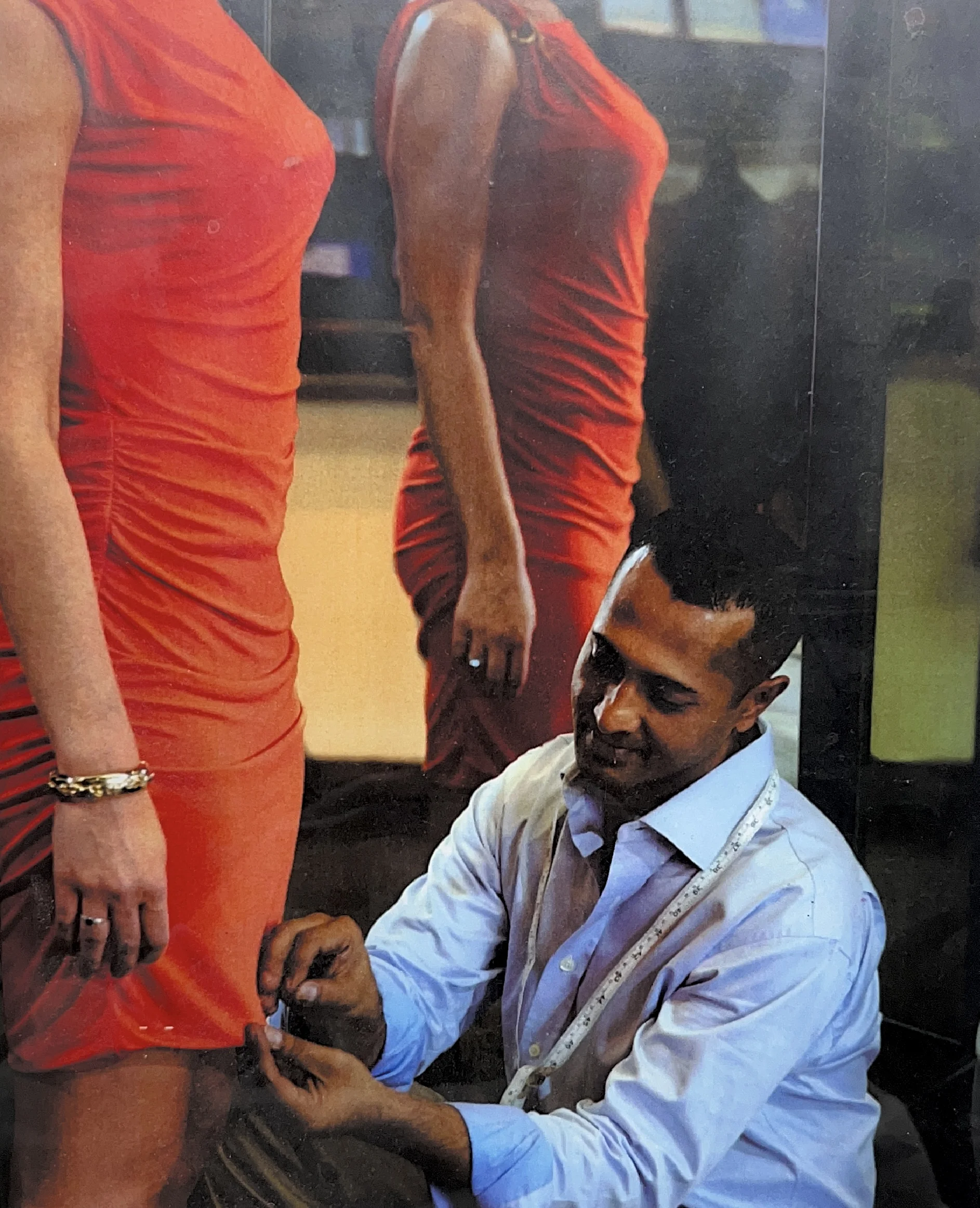 Tailor kneeling and pinning the hem of a woman's fitted red dress.