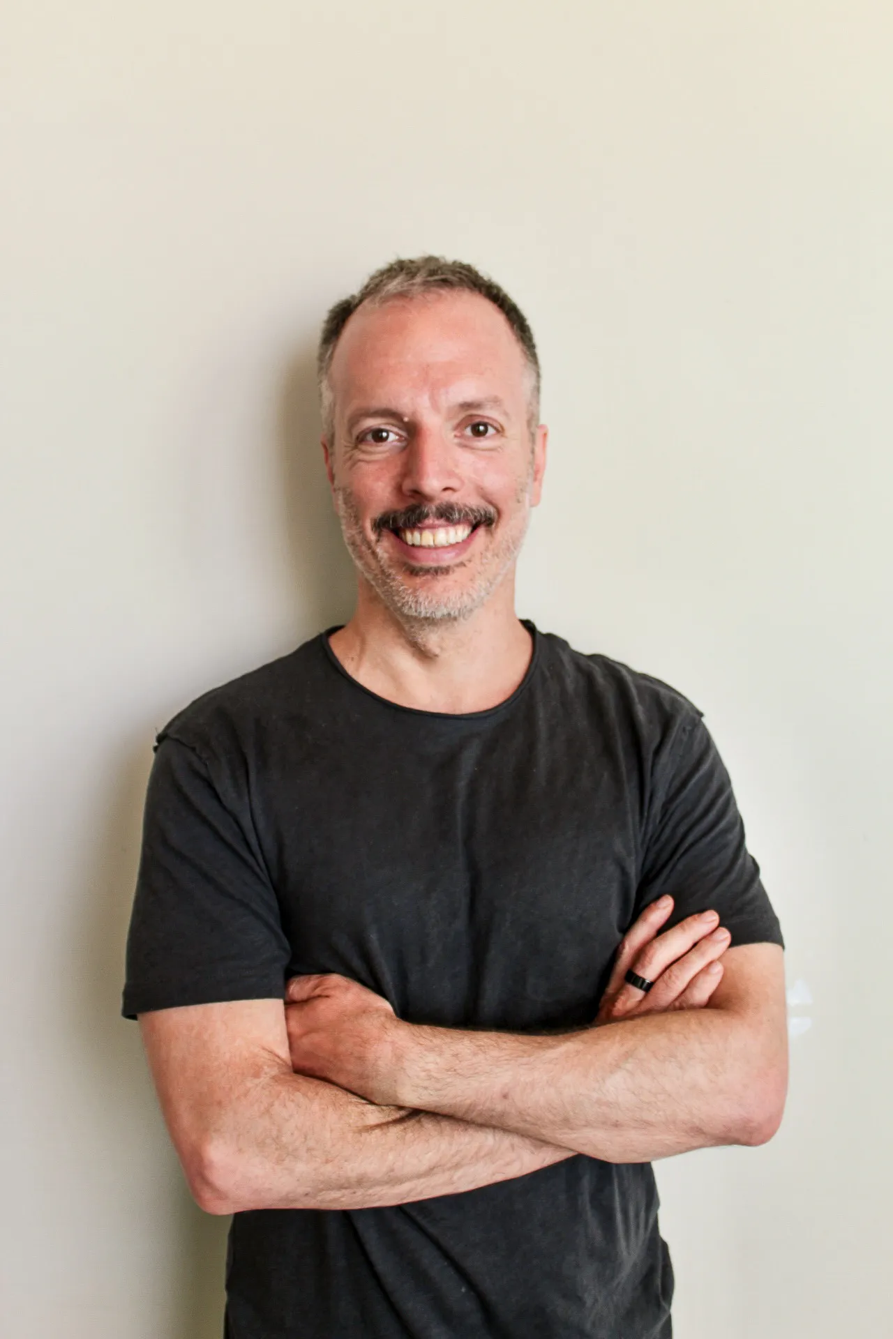 A man standing with his arms crossed in front of a white wall.