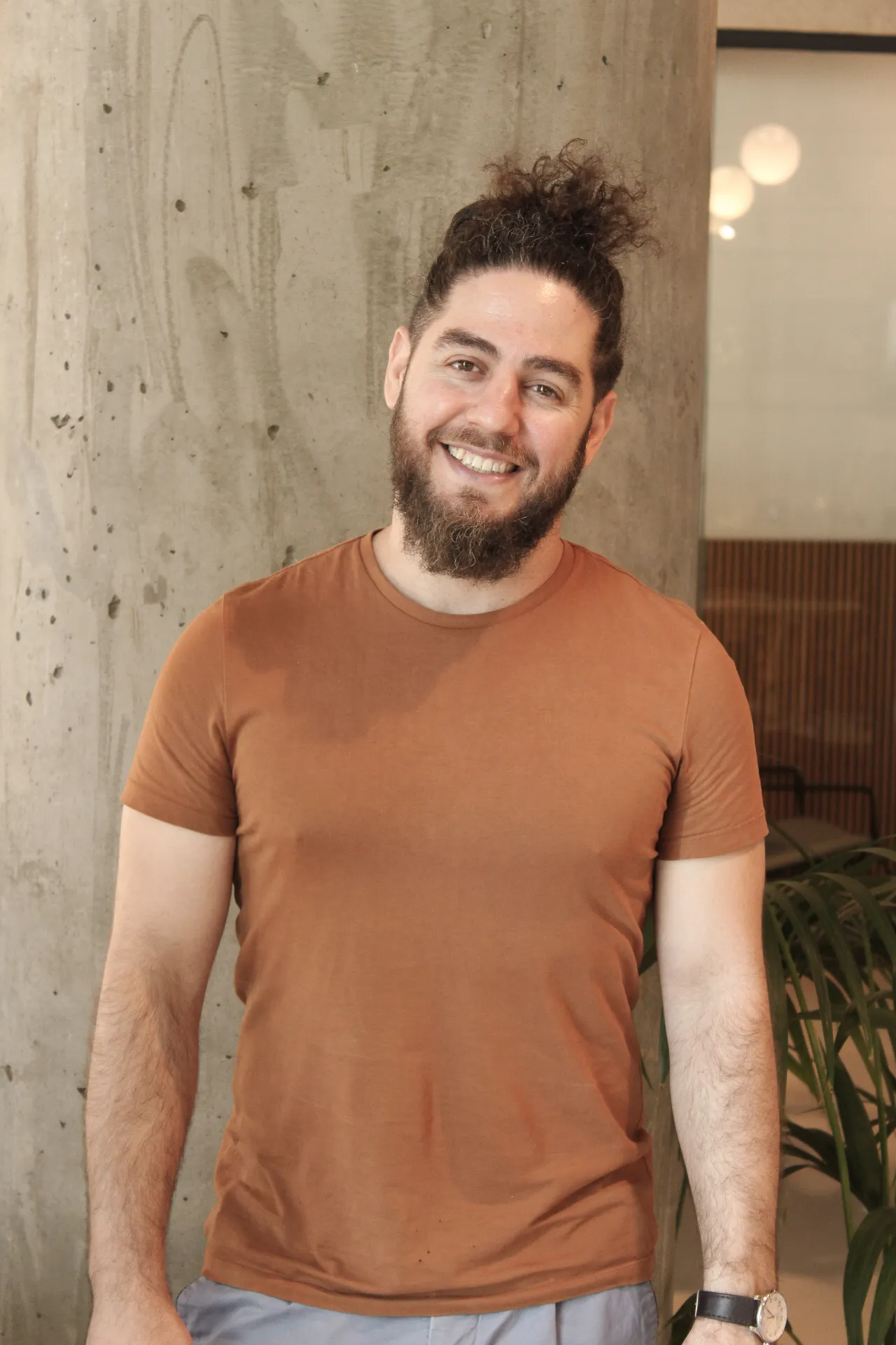 A man with a beard standing next to a plant.