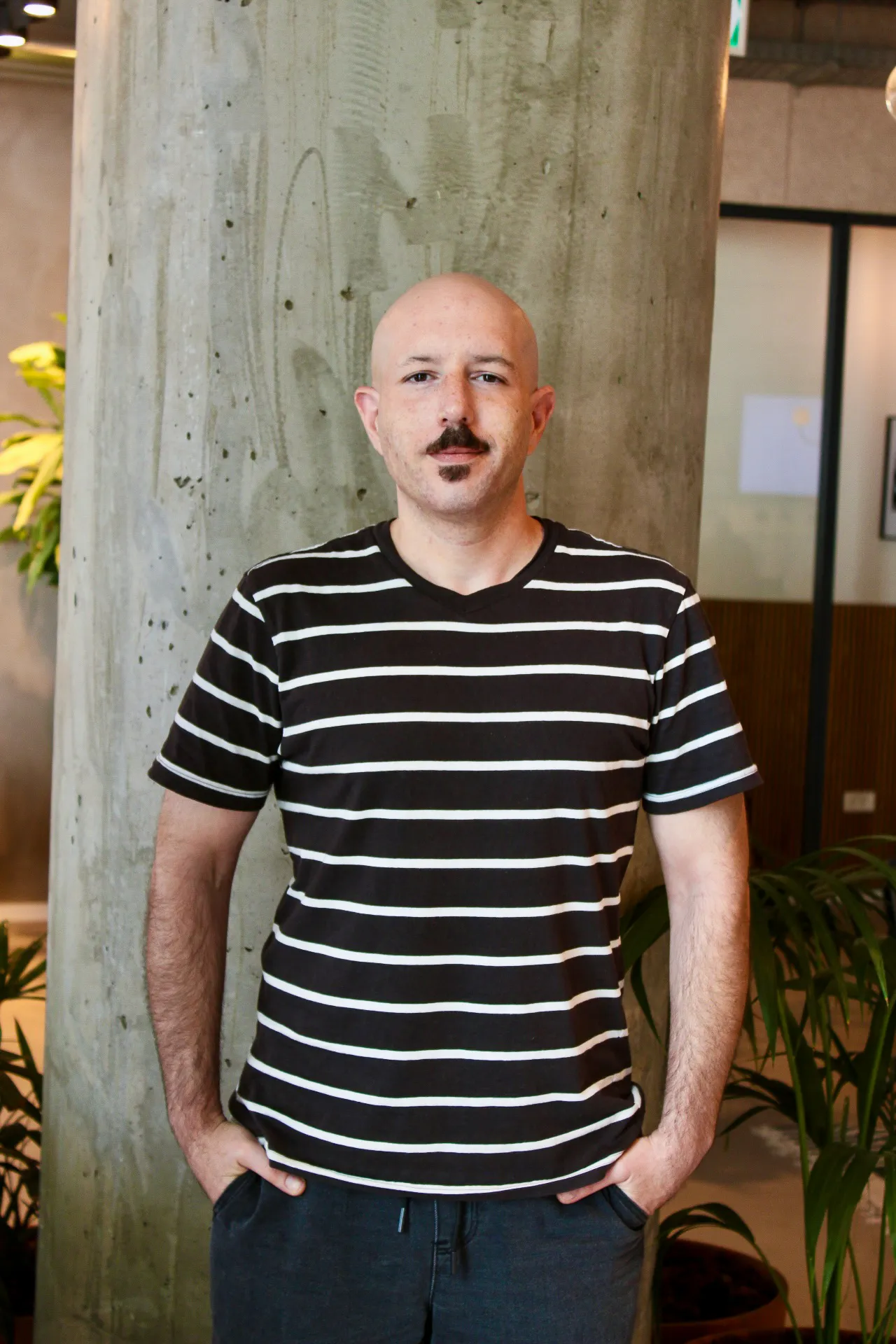 A bald man with a mustache standing in front of a tree.