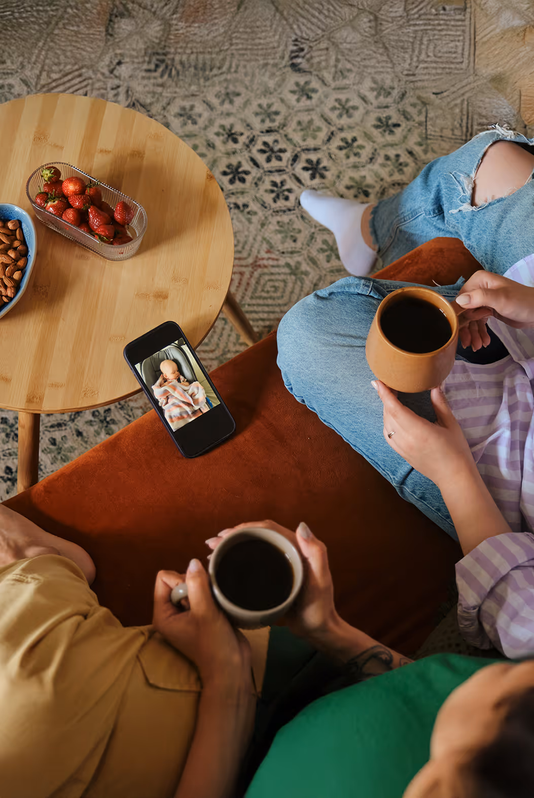 Two people drinking coffee next on the couch next to a phone.