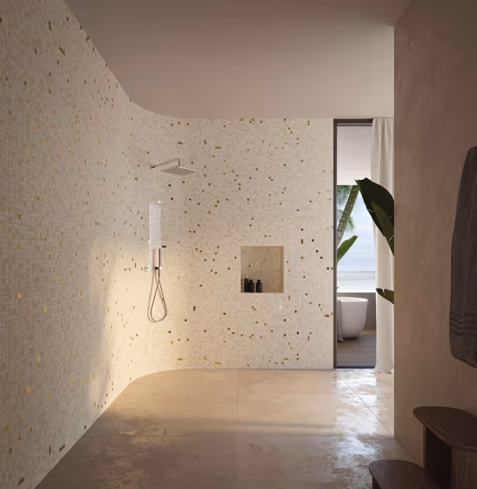 Modern bathroom with a spacious walk-in shower featuring beige mosaic tiles with gold accents, a built-in niche with black bottles, and a view of a bathtub by the window overlooking palm trees and the ocean.