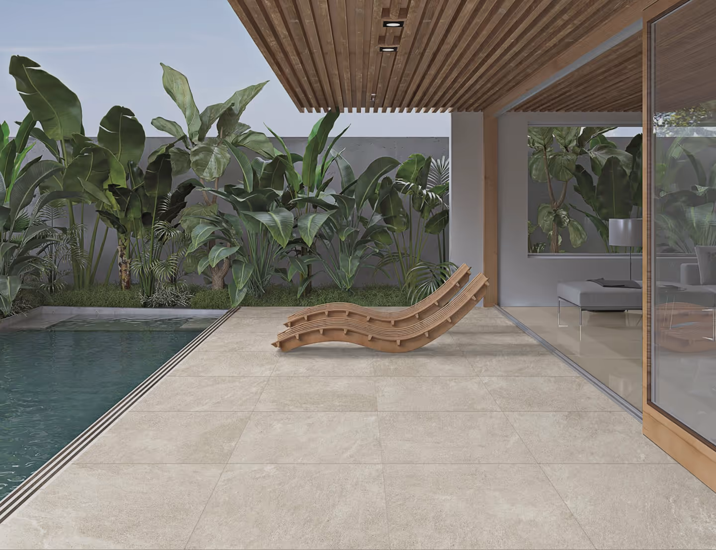 Outdoor patio with beige stone tiles, two wooden lounge chairs, a swimming pool, and lush green tropical plants against a gray wall.