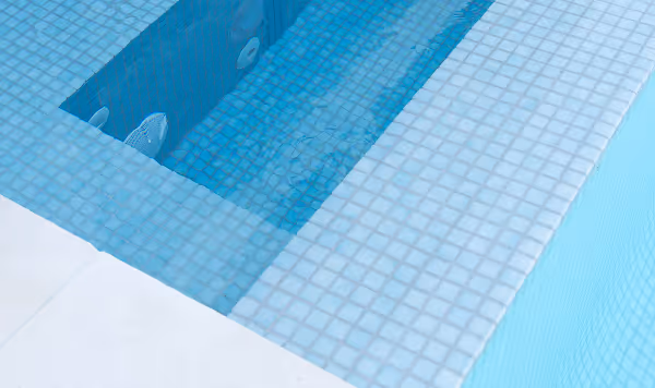 Close-up of a swimming pool corner showing blue mosaic tiles and clear water.