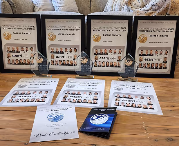Collection of framed 2022 Awards of Excellence from Swimming Pool & Spa Association of Australia for Europe Imports, including Business of the Year, Product of the Year, Best Supplier, and Sustainable Product Award, displayed with trophies and certificates on a wooden floor.