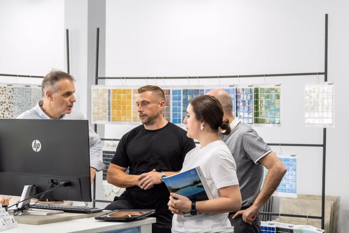 Four people discussing in an office with colorful tile sample boards in the background.
