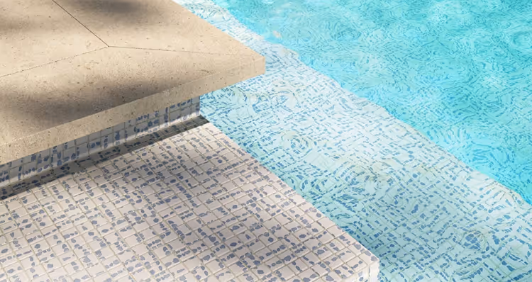 Close-up view of a pool edge with beige stone coping and light blue mosaic tiles underwater.