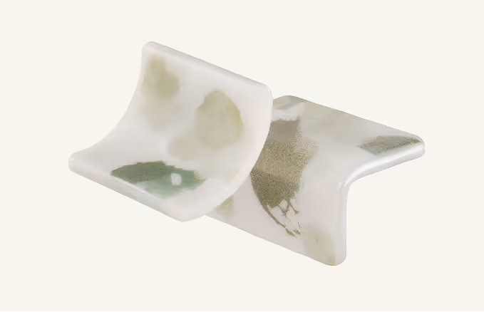 White ceramic object with greenish abstract pattern featuring a bent rectangular shape with curved edges.