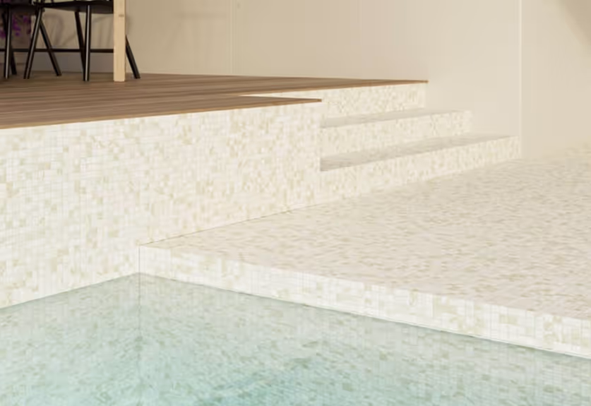 Close-up of a light beige tiled pool edge with steps leading up to a wooden deck with black chairs.