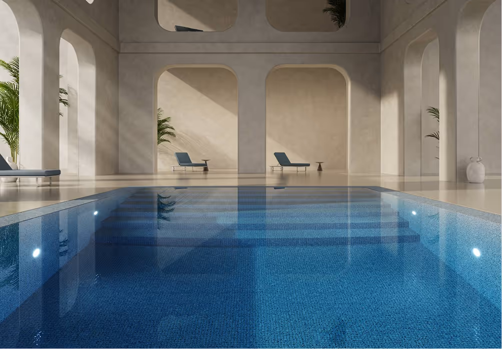 Indoor swimming pool with clear blue water, surrounded by beige walls with arches and lounge chairs.