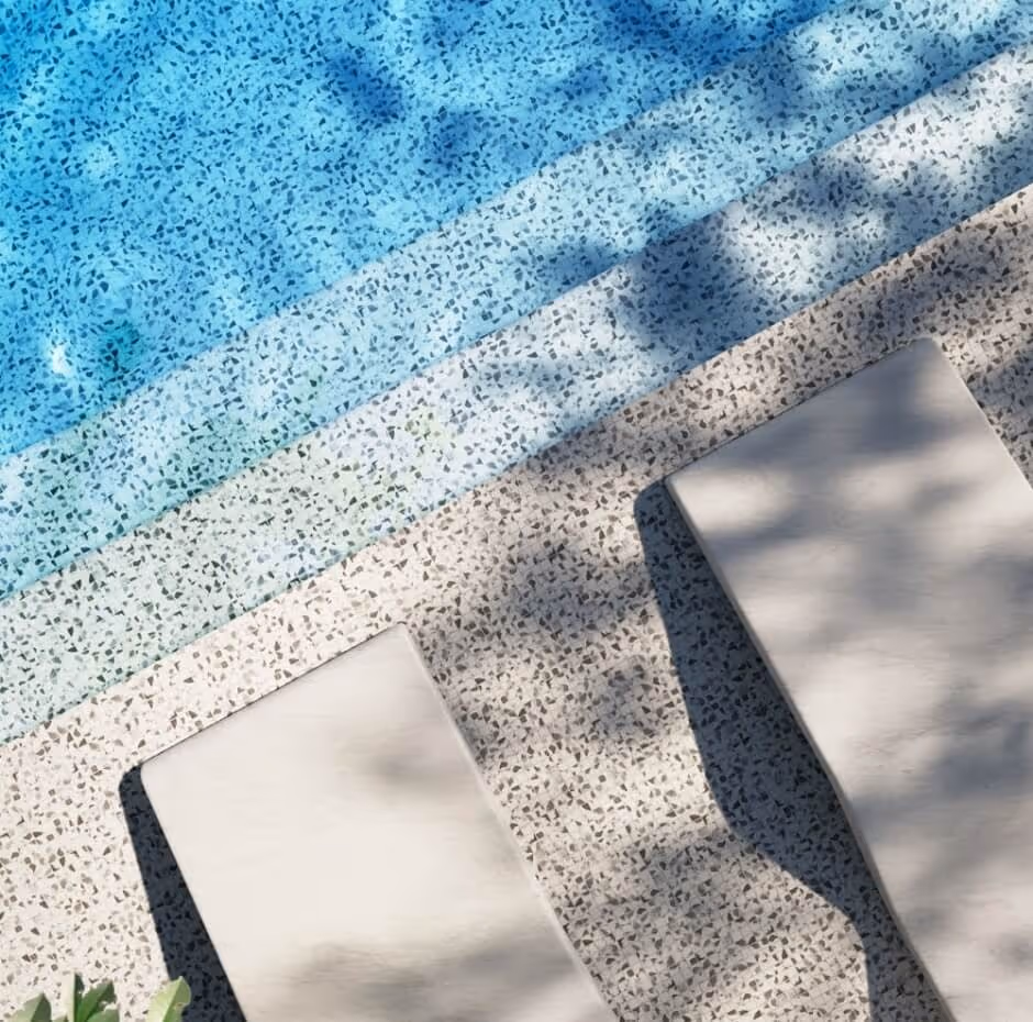 Blue swimming pool with mosaic tile pattern and two beige cushioned loungers on the stone pool deck.