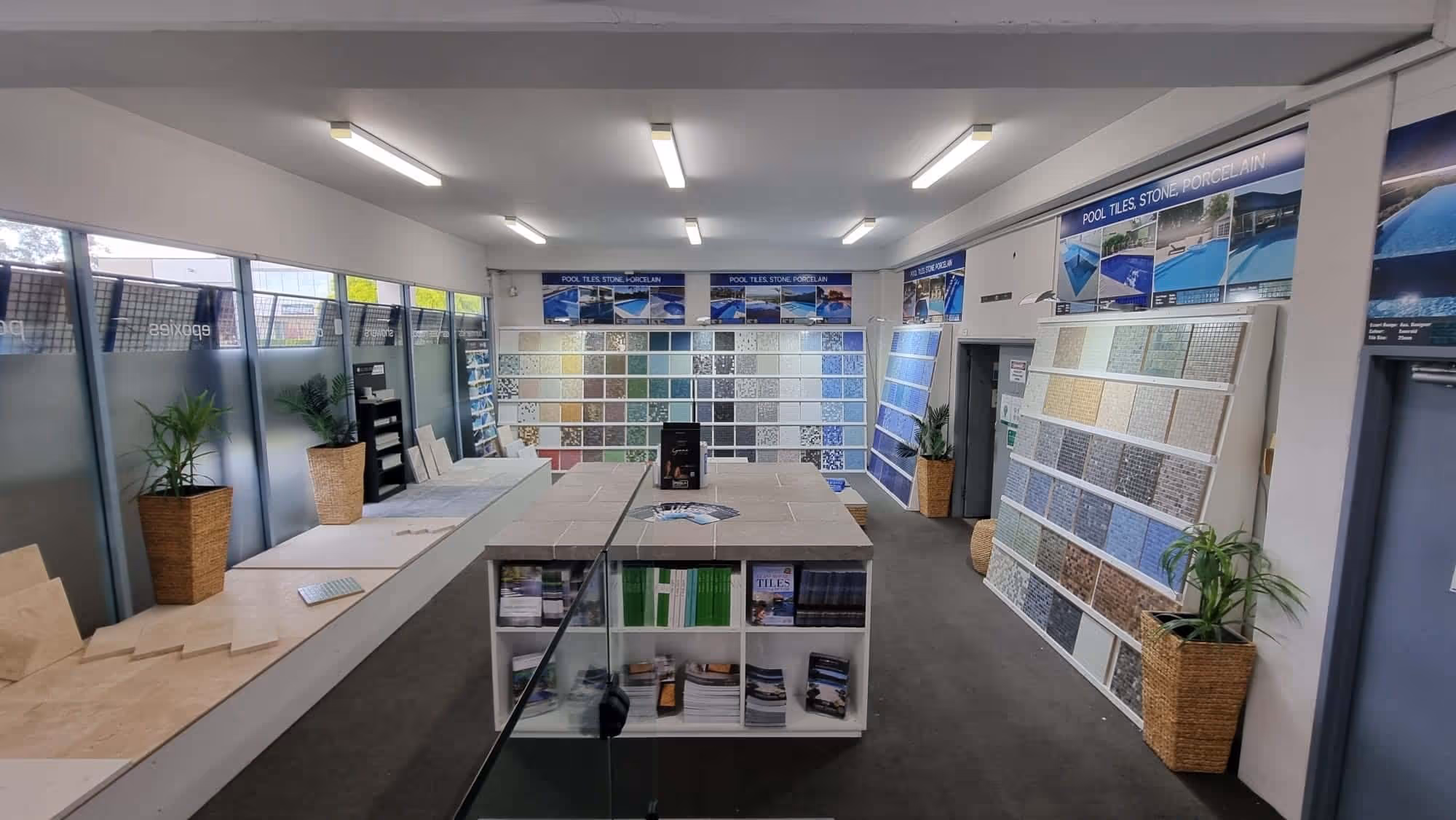 Showroom displaying various pool tiles, stone, and porcelain samples on panels and tables.
