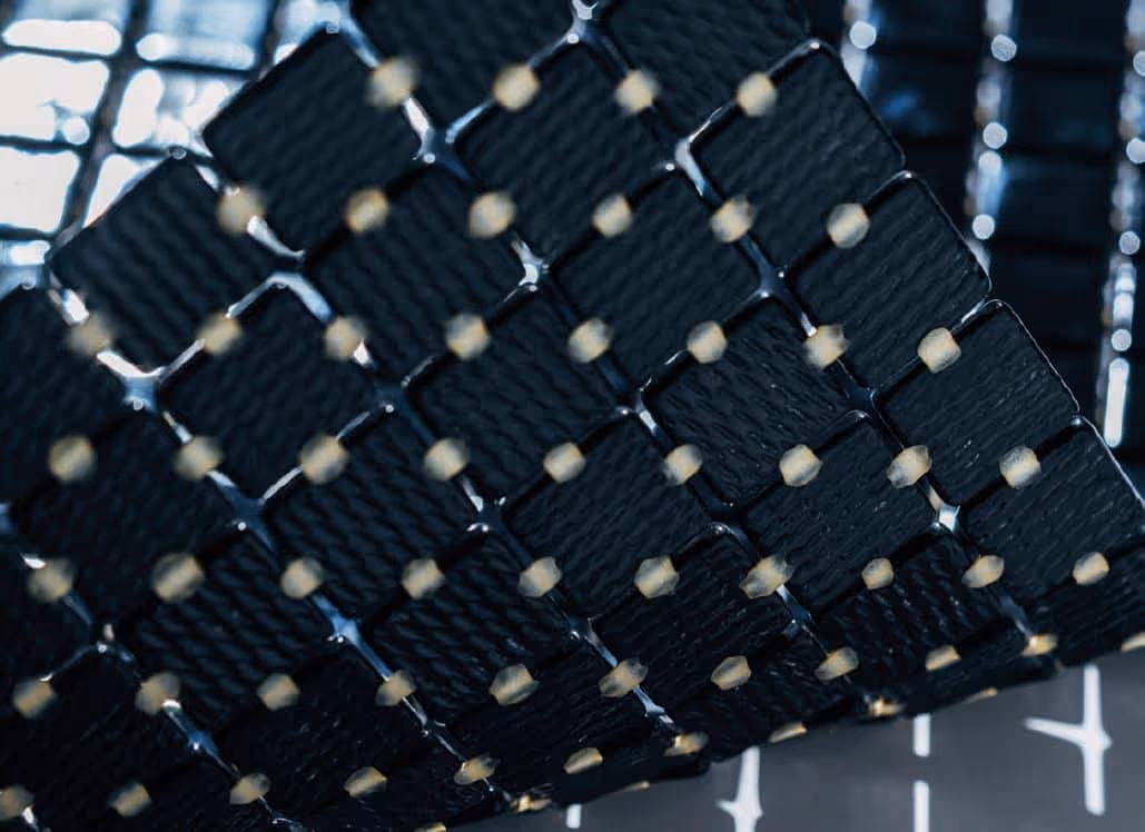Close-up of a hexagonal grid structure with black textured hexagonal tiles connected by small beige joints.