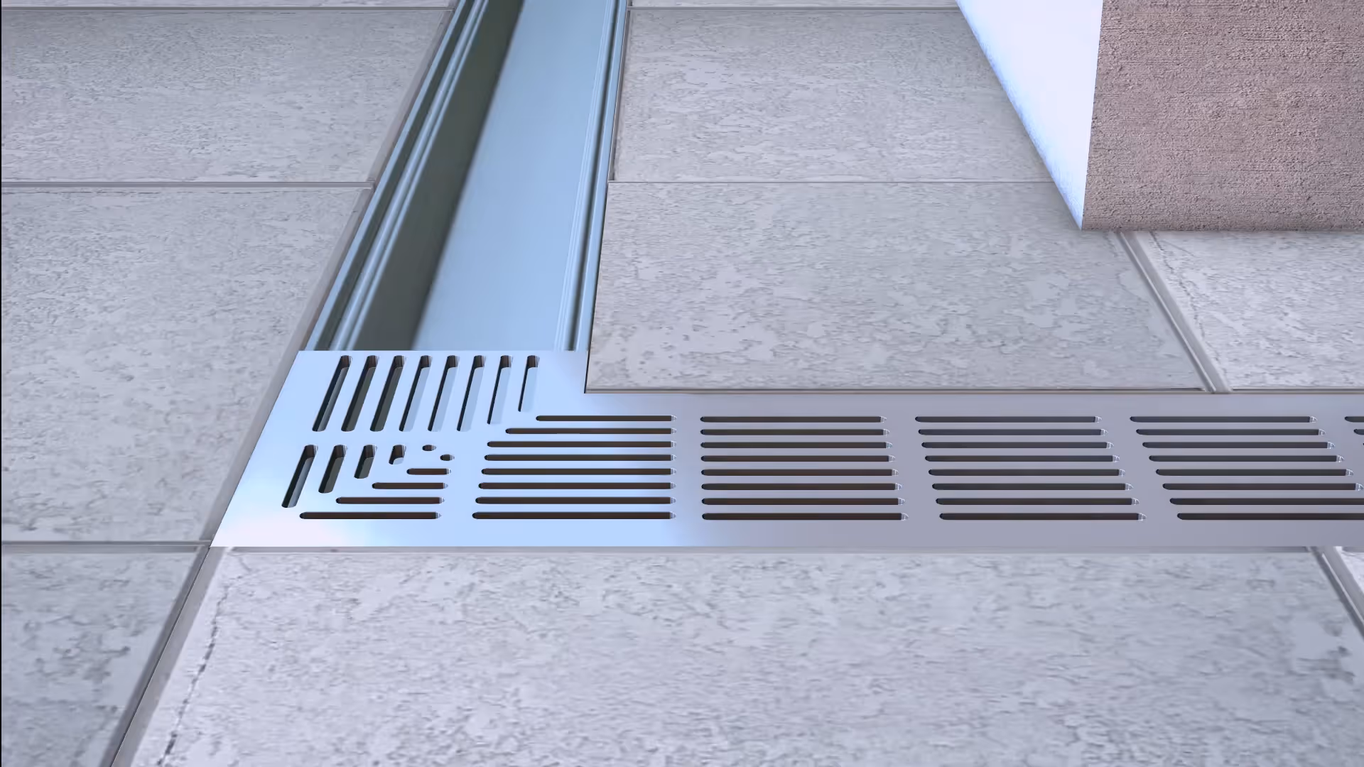 Close-up of a metal drainage grate installed flush with tiled floor next to a wall corner.
