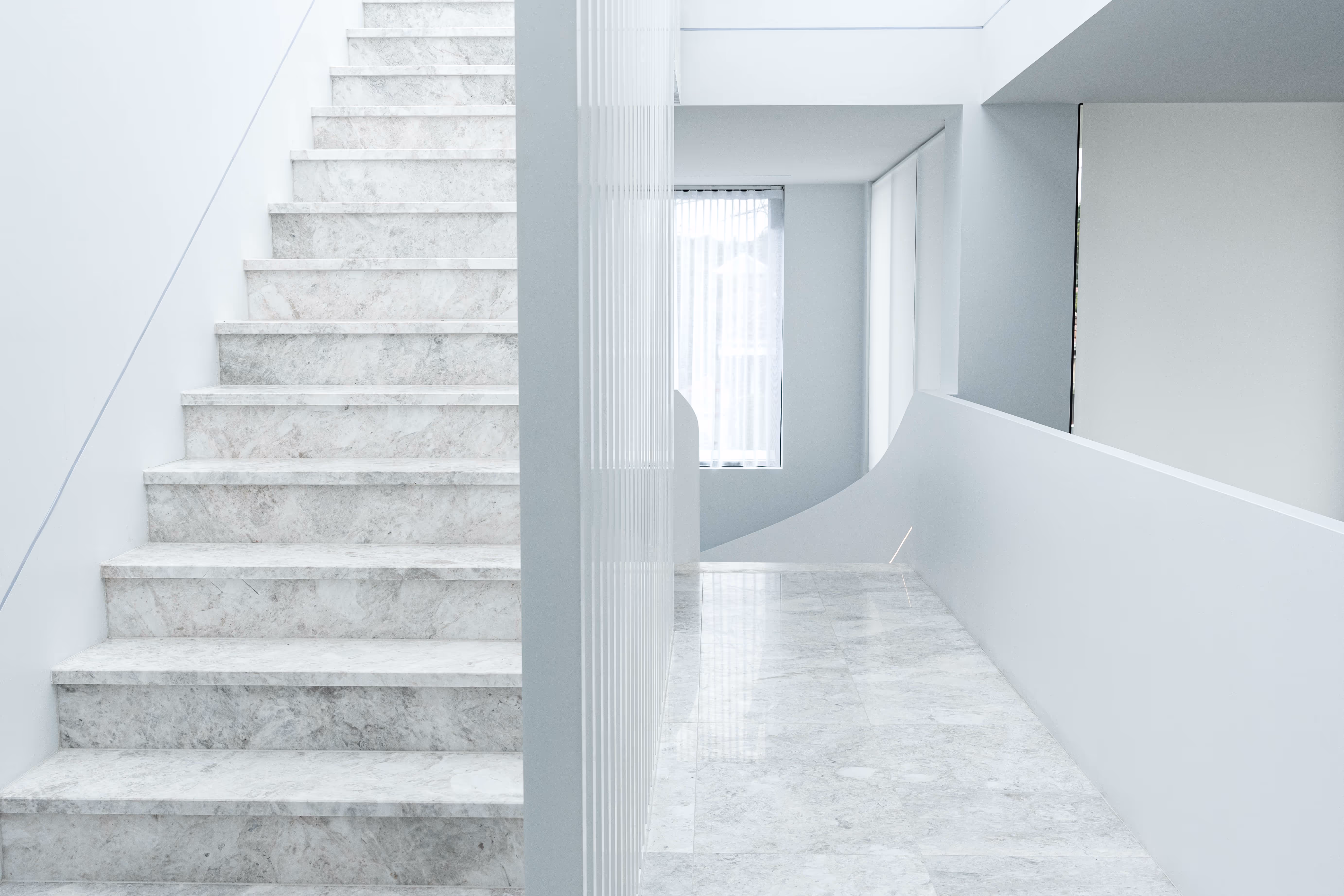 Modern white marble staircase with matching marble floor and minimalist white walls in a bright, airy interior.